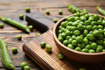 Bowl and board with fresh green peas on wooden background