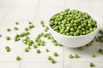 Bowl with fresh green peas on white tile background