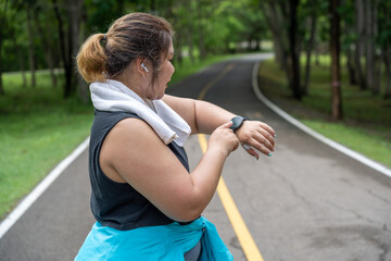 Young overweight woman checking the result of her morning run on her smart watch while standing at running track of a local park