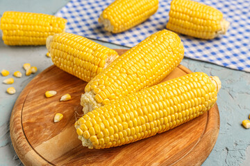 Wooden board with fresh corn cobs and seeds on blue background
