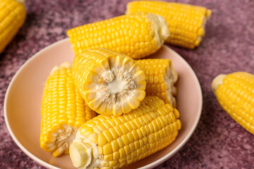 Bowl with cut fresh corn cobs on purple background