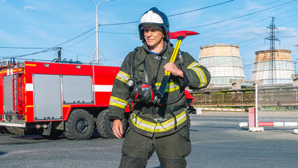 A lifeguard in protective clothing and helmet holds an axe on his shoulder. A firefighter next to a...