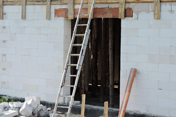 A ladder leaning against a wall, a rough window opening, reinforced brick lintels, walls made of autoclaved aerated concrete and wooden building props inside a house under construction