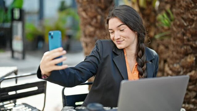 Young beautiful hispanic woman business worker make selfie by smartphone at coffee shop terrace