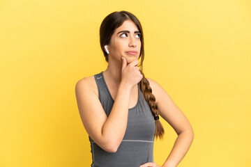 Sport caucasian woman isolated on yellow background having doubts
