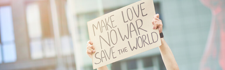 Save the world. Happy young male activist holding banner or poster over the head while protesting against war, standing on the road