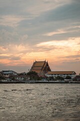 Fototapeta na wymiar Architectural structure is seen from the serene surface of a body of water at sunset in Bangkok