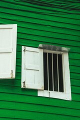 Vertical shot of open white windows on a green wall