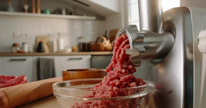 Electric meat grinder mince beef and pork meat in the kitchen in daylight. Soft blurred background slow motion camera zoom. Advertising Process of meat grinding with mincing electric machine Cook food