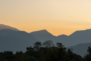 Breathtaking sunset over a rolling landscape of hills and lush green trees in the foreground