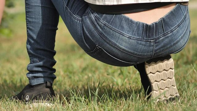 A woman in jeans squats and sits on a heel with her butt. sexy woman holding hands on her waist wearing blue jeans. Woman hand holding her bottom because having Abdominal pain