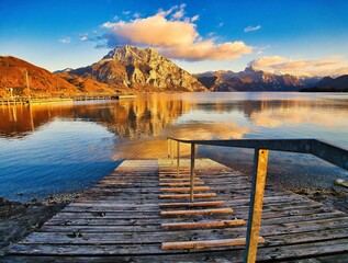 Obraz premium Scenic view of a wooden platform over the calm Traunsee lake against mountain landscape in Austria