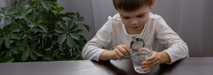 the child looks at the water through a magnifying glass. Selective focus.