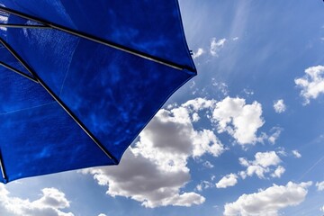 Closeup of a blue umbrella against a backdrop of a blue sky with white clouds