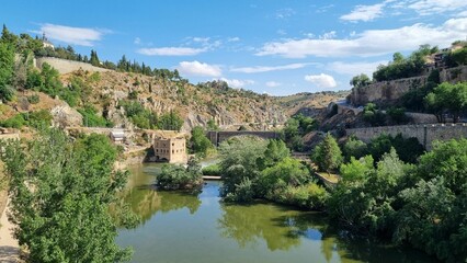 Fototapeta na wymiar Scenic view of a large river surrounded by lush green hills in Toledo, Spain.