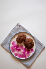 Brown muffins with pink rose petals on a light blue dish towel top flat lay