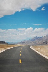 Vertical of an empty highway alongside the wide field with big mountains in the background