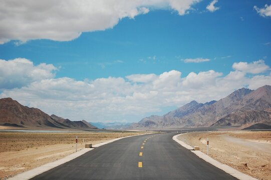 Empty highway alongside the wide field with big mountains in the background