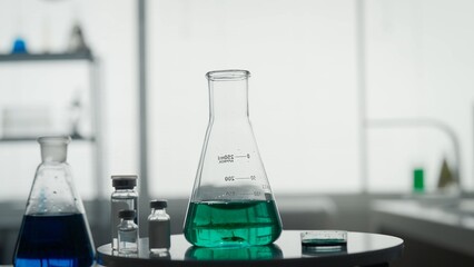 Scientific experiment. A Erlenmeyer flask with a green liquid on the table on a blurred laboratory background close up.