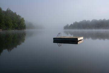 Wooden raft floating on a quiet lake in Quebec, Canada with mist rising in the background.