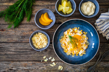 Fruit salad - peaches, pineapples, almonds and corn in mayonnaise on wooden table