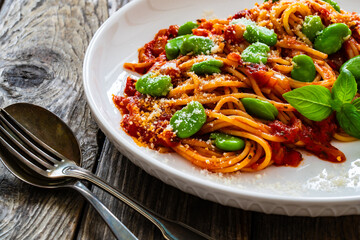 Spaghetti in tomato sauce with broad bean, parmesan cheese and basil leaves on wooden table
