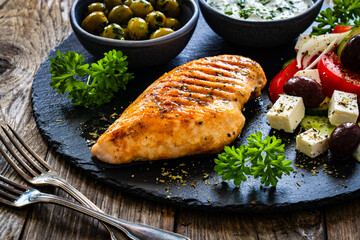 Seared chicken breast and Greek salad on wooden table
