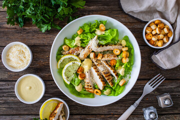Caesar salad - fried chicken breast and vegetables on wooden table
