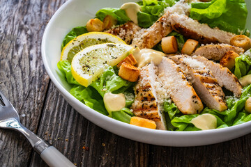 Caesar salad - fried chicken breast and vegetables on wooden table
