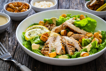 Caesar salad - fried chicken breast and vegetables on wooden table
