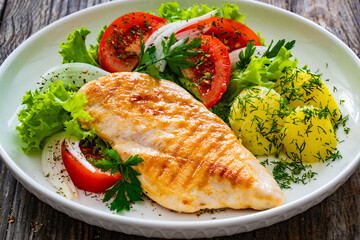 Grilled chicken breast, boiled potatoes and fresh vegetables on wooden table

