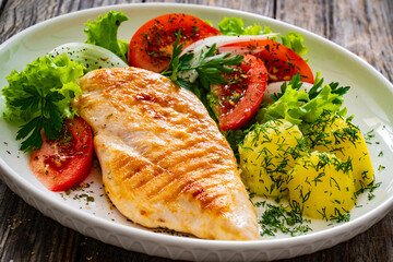 Grilled chicken breast, boiled potatoes and fresh vegetables on wooden table
