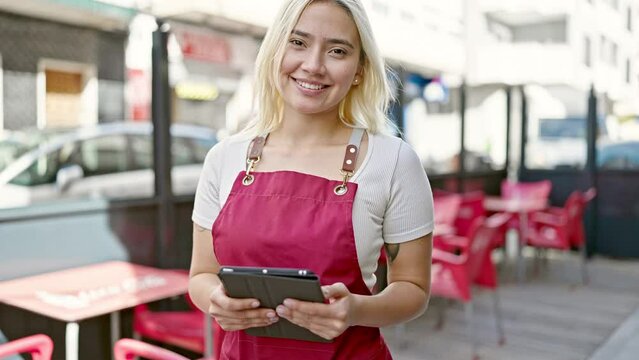 Young beautiful hispanic woman wearing apron using touchpad at coffee shop terrace