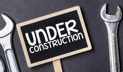 Under construction text written on a small chalk board and black background.