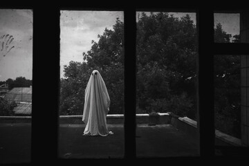 Ghost in a sheet on the roof of an old abandoned house view through the window, spooky Halloween...