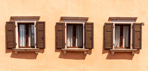 Fototapeta na wymiar old yellow facade of house with three brown vintage wooden windows in retro italian european style