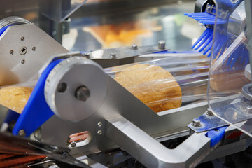 baked bread in food grade plastic bag on conveyor belt moves to seal in packing machine at...