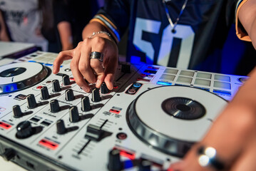 A cool DJ standing at the mixer controller, composing a new mix and making the party in a nightclub...