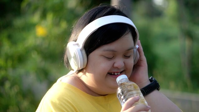  While exercising in the park, an Asian girl with down syndrome uses a water bottle as a microphone.