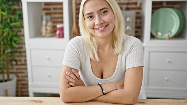 Young beautiful hispanic woman smiling confident sitting on table with arms crossed gesture at dinning room