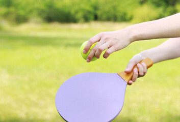 Play paddleball in the park. Hands with a wooden paddle for playing beach tennis close-up. Outdoor games. The girl is preparing to hit the ball with a racket