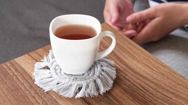 Young female friends-colleagues chat over a cup of hot tea on the couch. A cup of tea stands on a do-it-yourself knitted stand