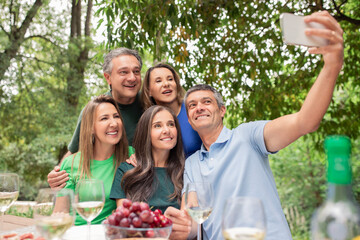 Group of mature friends taking selfie with smartphone and making barbecue outdoors