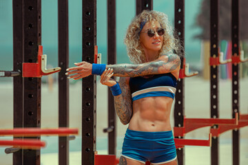 Muscular young woman stretching arms after exercise at sports ground. Stunning girl with curl hair...