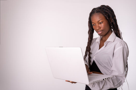 Cuerpo entero de una joven exitosa mujer de color de negocios empleada que usa una camisa blanca y una falda negral con una computadora port&aacute;til en las manos y una mirada al ordenador.