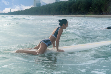 Asian girl sporting and surfing as a hobby, practicing surfing lie down and stand up on a board in the sea Waiting for the big wave to stand on the board until the sun goes down