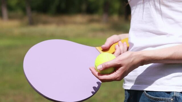 Play paddleball with a wooden racket on the background of nature. A wooden paddle for playing tennis and a ball in the hands of a girl. Outdoor games. Close-up