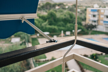 Terrace of a beach apartment with the awning down. Image of a sunshade system composed of a blue awning and a white handle to operate it. - obrazy, fototapety, plakaty