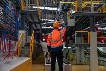Caucasian man wearing safety uniform and helmet standing hand signaling for trains to enter the tracks to inspect trains for maintenance at the train depot.