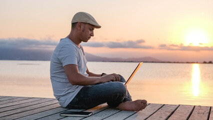 Male freelancer working on pier. Remote worker at sunset